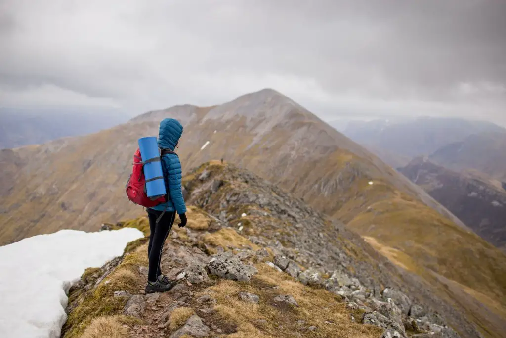 Person auf dem Gipfel des Berges mit rotem Rucksack